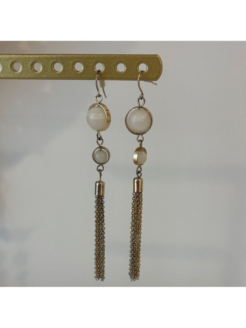 Gold toned dangle earrings with white cabochon-style stones and chain tassels